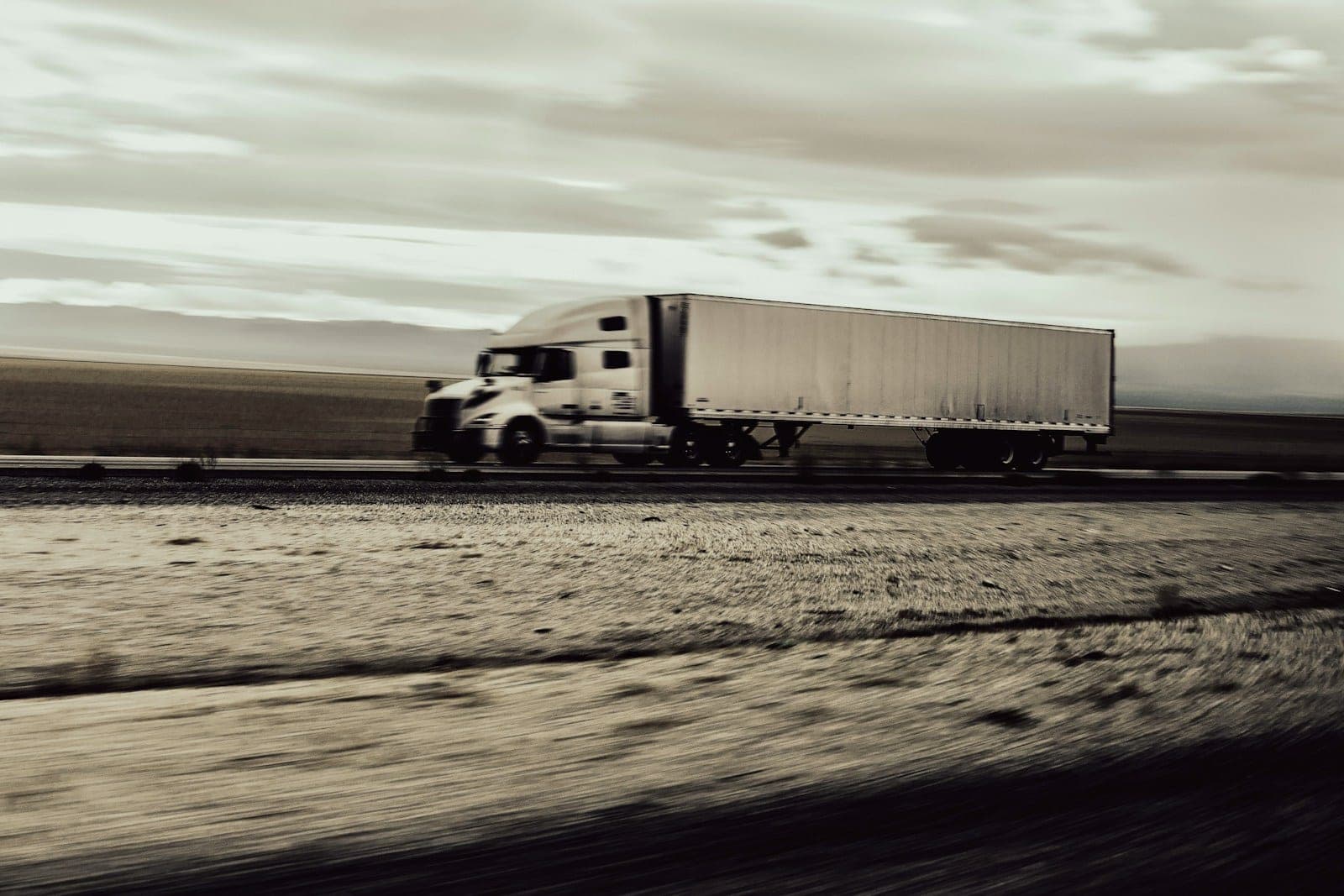 A tractor-trailer photographed while panning alongside it on an open road, the ground blurred by the movement.